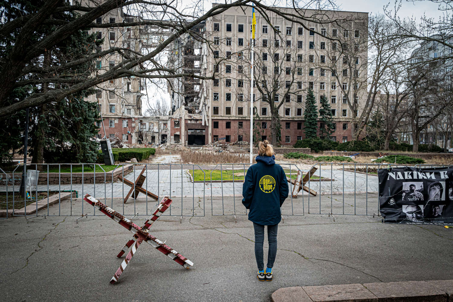 Age of Hope volunteer viewing ruins of a bombed building behind tank barriers